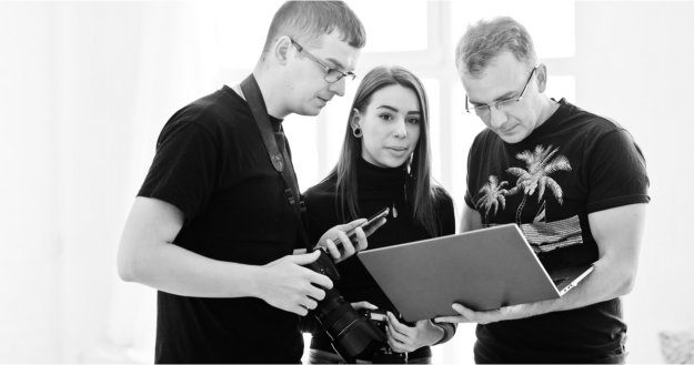 שלושה אנשים צעירים יושבים סביב שולחן עם מסמכים פיננסיים, מחייכים ומתכננים איחוד הלוואות